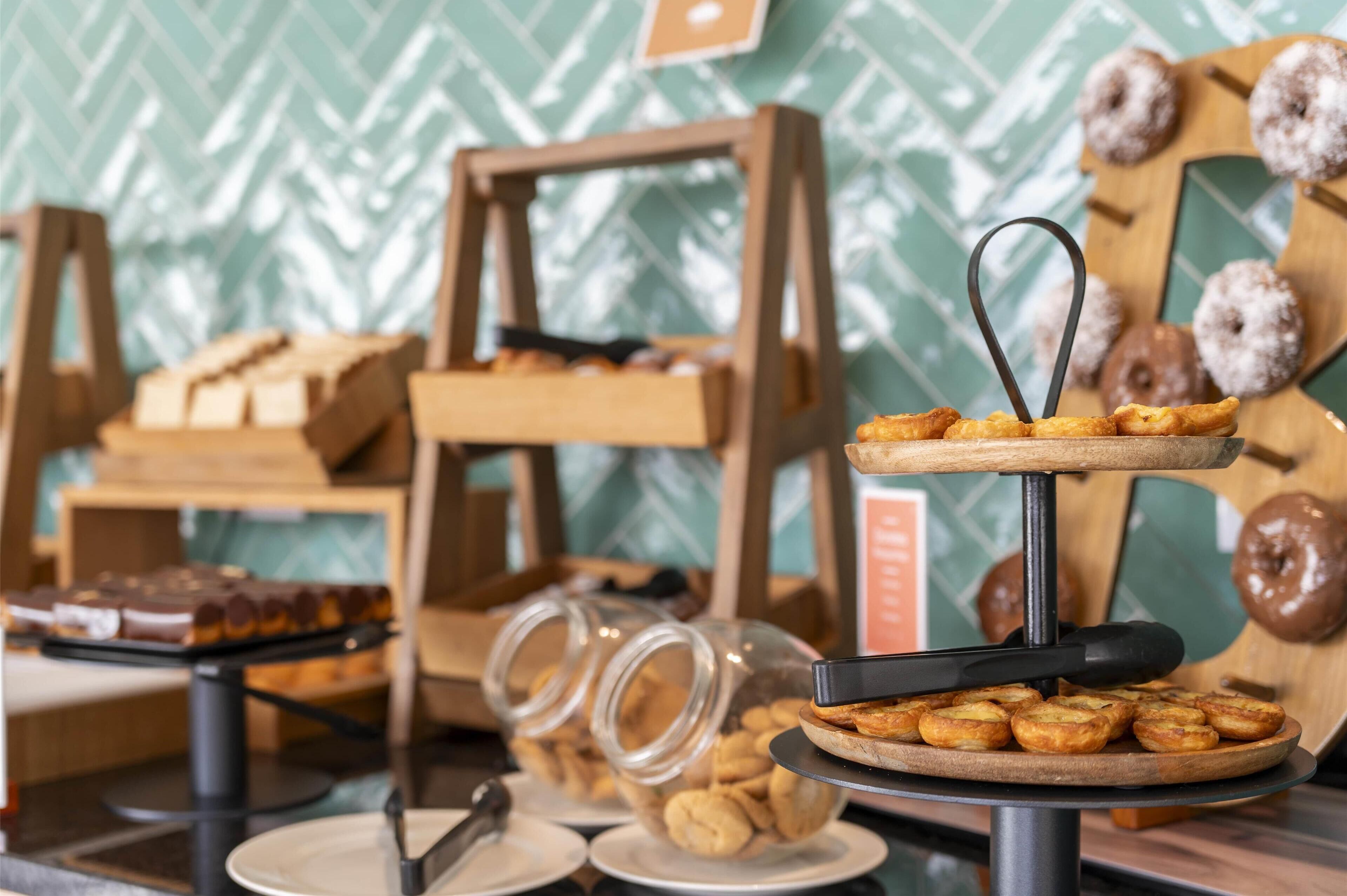 Un bufé con diversas opciones de pastelería y postres, incluyendo rosquillas y galletas, exhibido sobre soportes de madera y un plato giratorio.