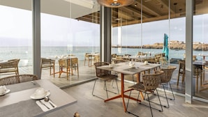 Un comedor moderno con mobiliario de mimbre, ventanas amplias y vistas al mar.