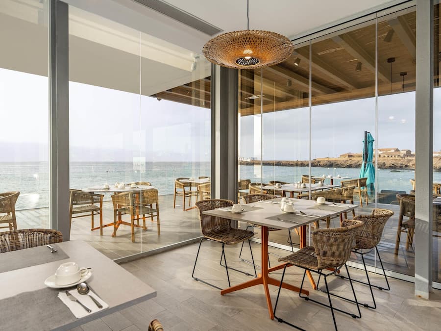 Un comedor moderno con mobiliario de mimbre, ventanas amplias y vistas al mar.