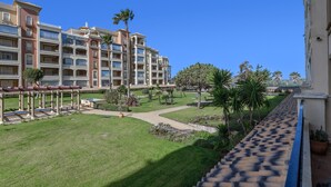 Une cour d’hôtel avec une piscine, des palmiers et un ciel d’un bleu limpide.