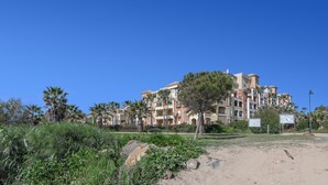 Un immeuble résidentiel à plusieurs étages, doté de balcons et entouré de verdure et de palmiers.