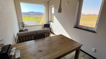 A room with a wooden table, a bench, and a view of a green field through large windows.