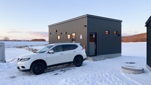 Ein weißer SUV parkt vor einem kleinen, modernen Gebäude mit einer Tür, auf der 'C' steht.