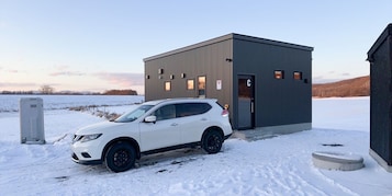 Un SUV blanco estacionado frente a un edificio pequeño y moderno con una puerta marcada 'C'.
