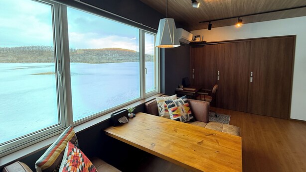 Ein modernes Interieur mit einem großen Fenster mit Blick auf einen See, einer hölzernen Bank sowie einem Essbereich mit Tisch und Stühlen.