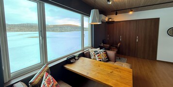 Un interior moderno con un ventanal grande con vistas a un lago, un banco de madera y una zona de comedor con mesa y sillas.