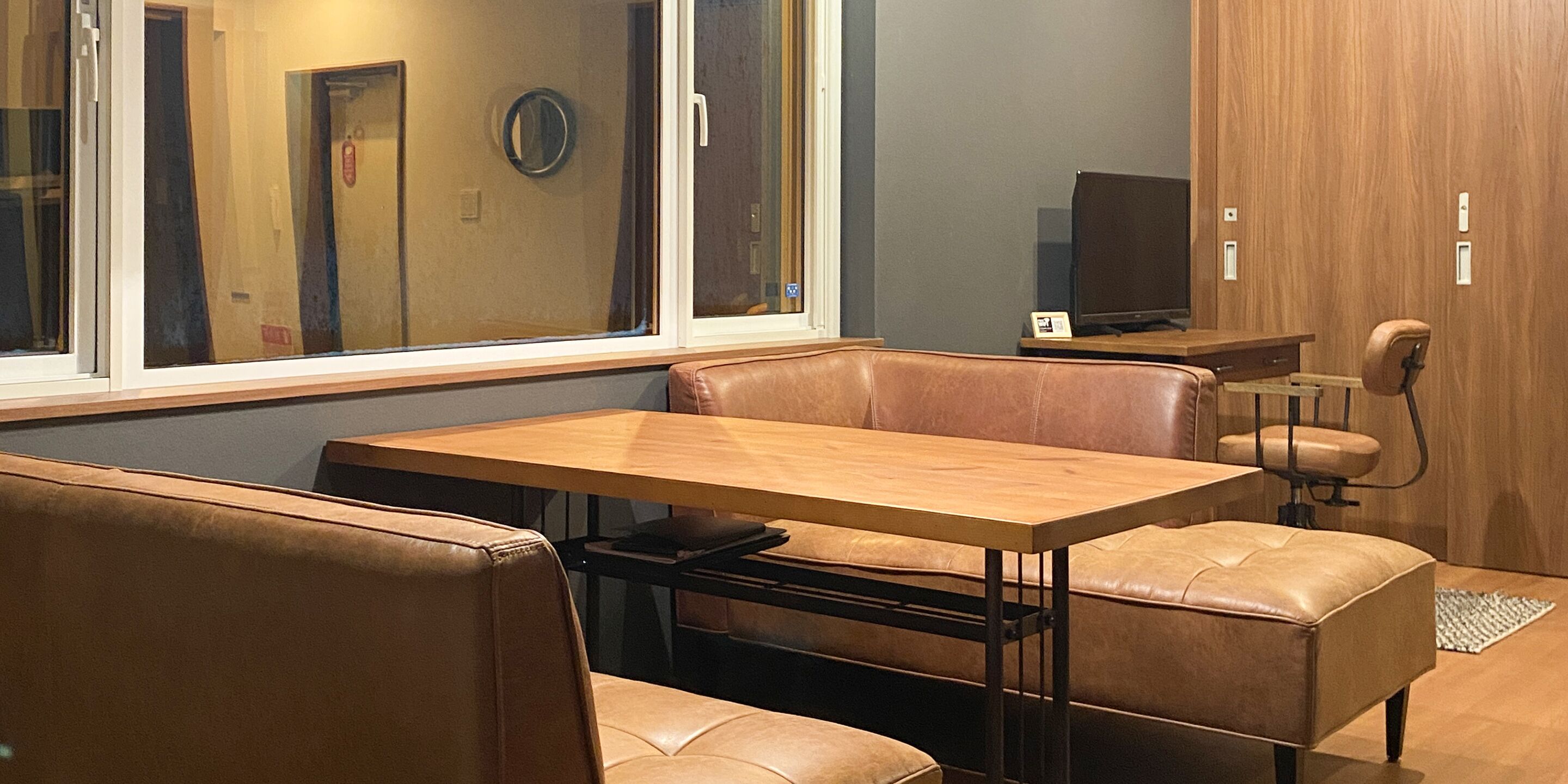 A modern room with a wooden table and leather seating, a television, and a large window.