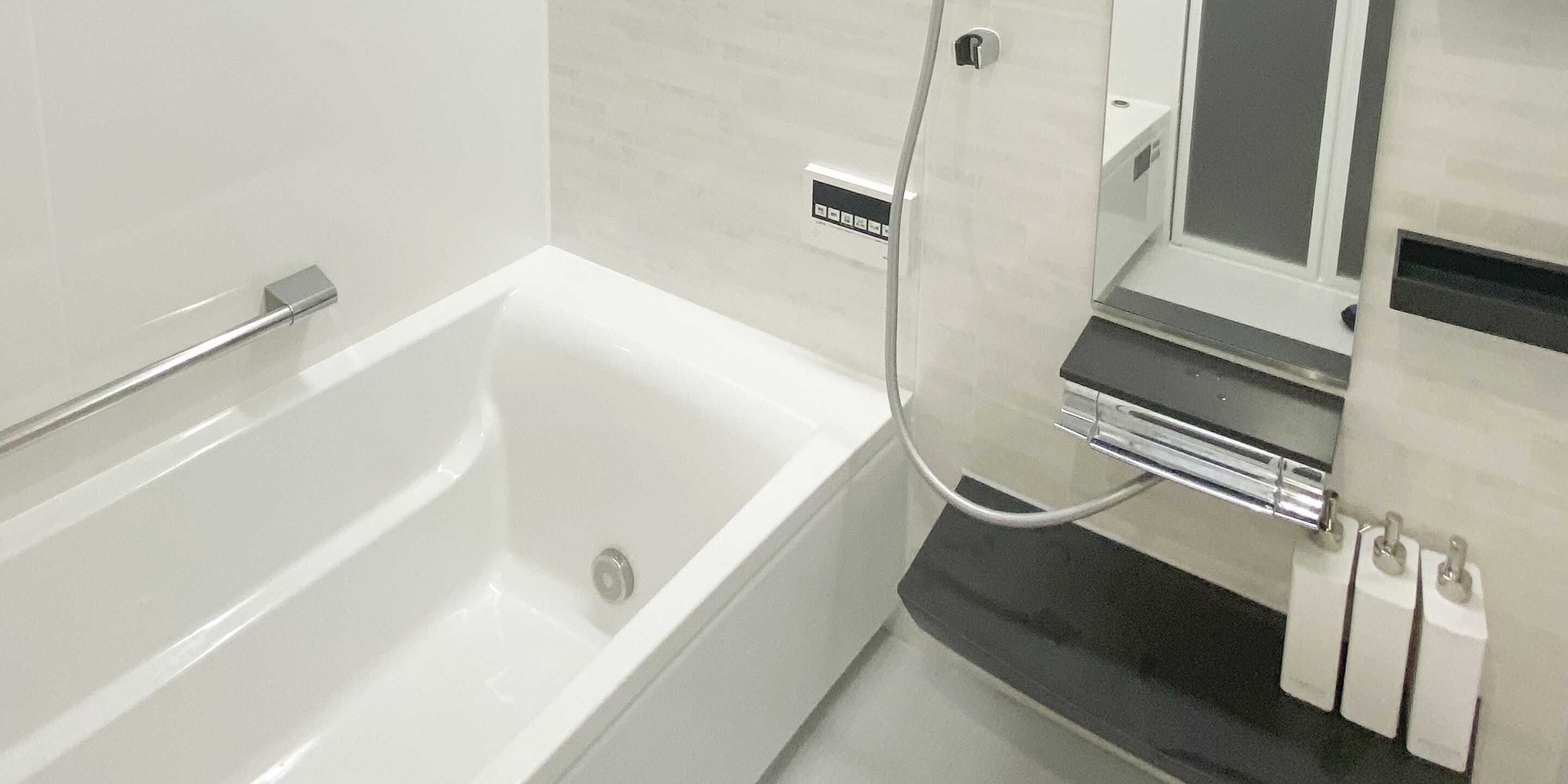 A modern bathroom with a white bathtub, a handheld showerhead, and a black countertop with a mirror and three white soap dispensers.