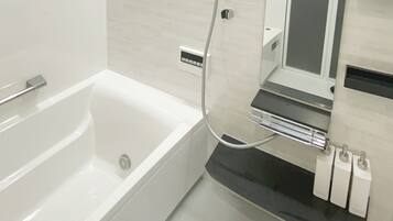 A modern bathroom with a white bathtub, a handheld showerhead, and a black countertop with a mirror and three white soap dispensers.