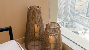 Two tall, cylindrical wicker lamps with a warm light inside, placed on a balcony with a city view. - Luxe High Floor In Address Marina.36 (Dubai)
