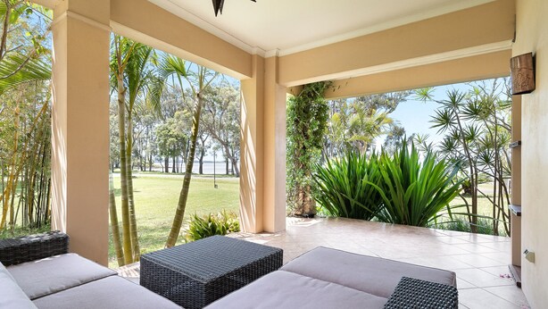 A covered patio area with wicker furniture and a view of a lush garden.