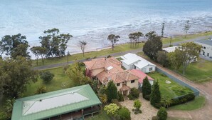 A coastal property with a house featuring a red-tiled roof, a green-roofed structure, and a view of the sea.