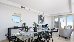Un comedor moderno con una mesa de vidrio, sillas negras y un espejo redondo en la pared.