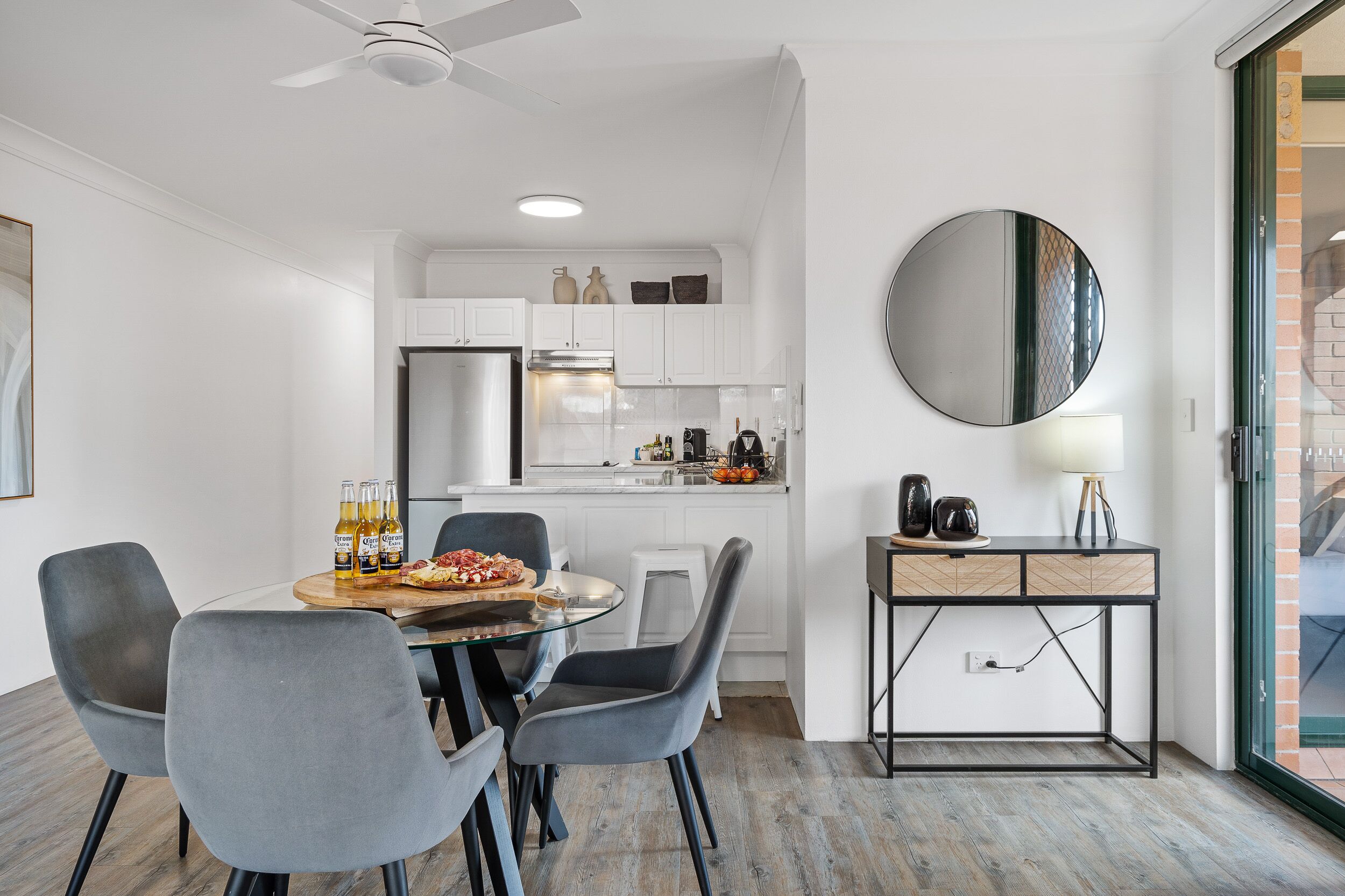 A modern kitchen with white cabinets, a dining area with grey chairs, and a round mirror on the wall.