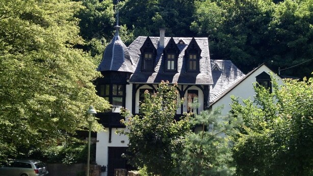 Une maison traditionnelle avec un toit à forte pente, plusieurs cheminées et une façade blanche.