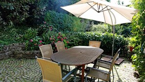 Une table ronde en bois, six chaises en osier et un parasol beige.