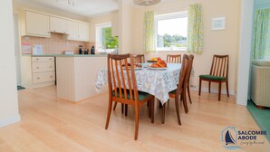 A spacious kitchen with wooden cabinets, a dining table with chairs, and a view of greenery outside. - Detached 4 bed Coastal Haven  | Garden  |  Parking (Salcombe)