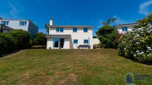 A two-story house with a front door, a patio with a table and chairs, and a well-maintained lawn. - Detached 4 bed Coastal Haven  | Garden  |  Parking (Salcombe)