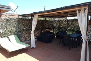 An outdoor patio with lounge chairs, a table, and a covered seating area.