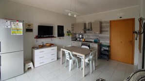 A modern kitchen with white cabinets, a dining table with chairs, a refrigerator, and a television on the wall. - Casa Leto 5 (Letojanni)