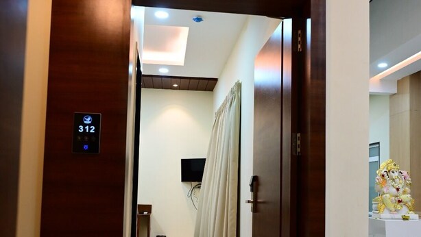 A hotel corridor with a wooden door, a digital elevator display, a television, and a decorative statue. - Unnati Stays Inn, VIJAYAPUR (VIJAYAPUR)