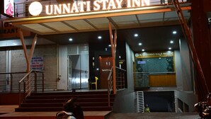 The exterior of the Unnati Stay Inn, featuring a prominent illuminated sign, a staircase leading to the entrance, and a visible restaurant sign in the background. - Unnati Stays Inn, VIJAYAPUR (VIJAYAPUR)