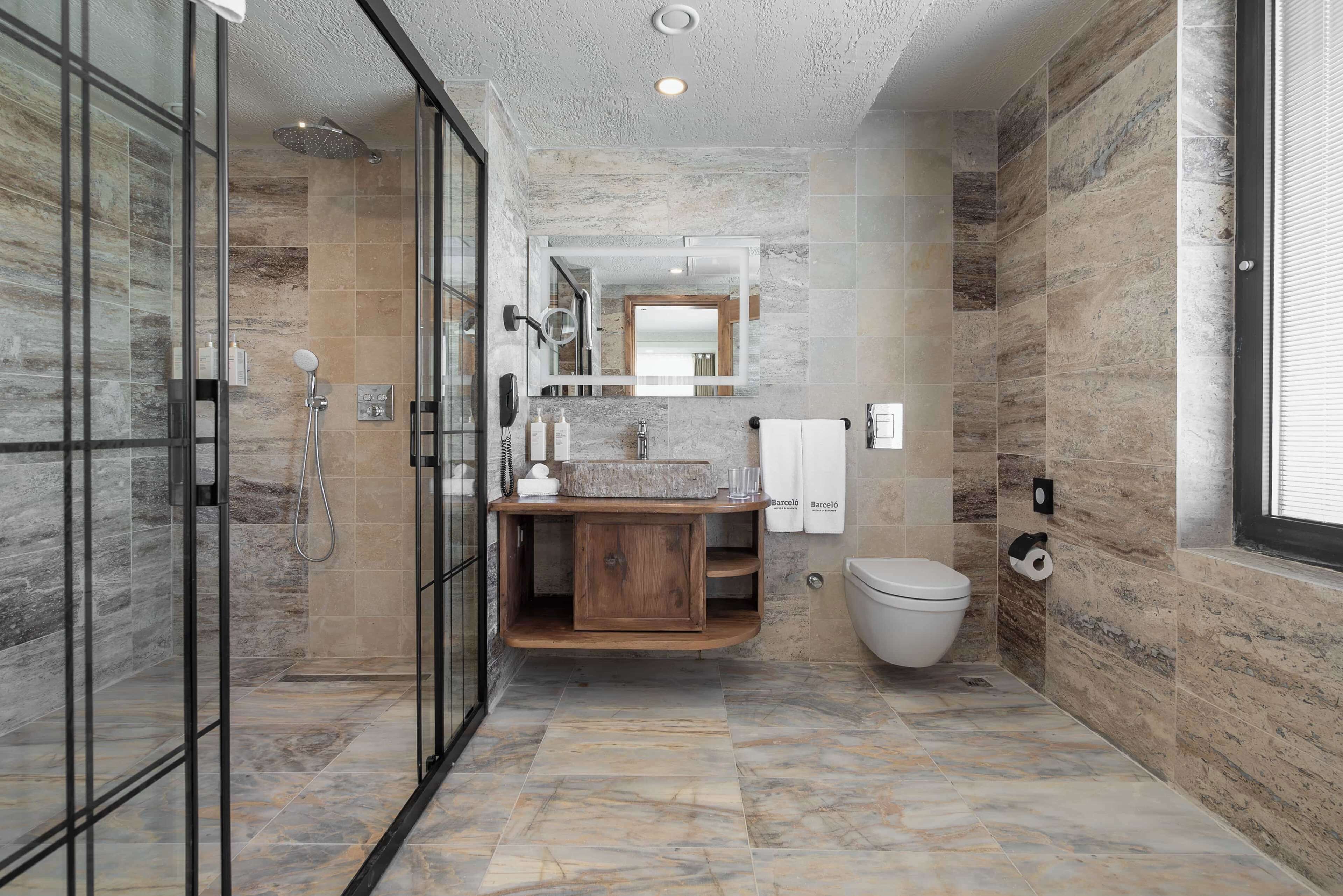 A modern bathroom with a glass shower enclosure, a wooden vanity, and a marble-tiled floor.