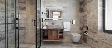 Un baño moderno con cabina de ducha de vidrio, tocador de madera y suelo de baldosas de mármol.