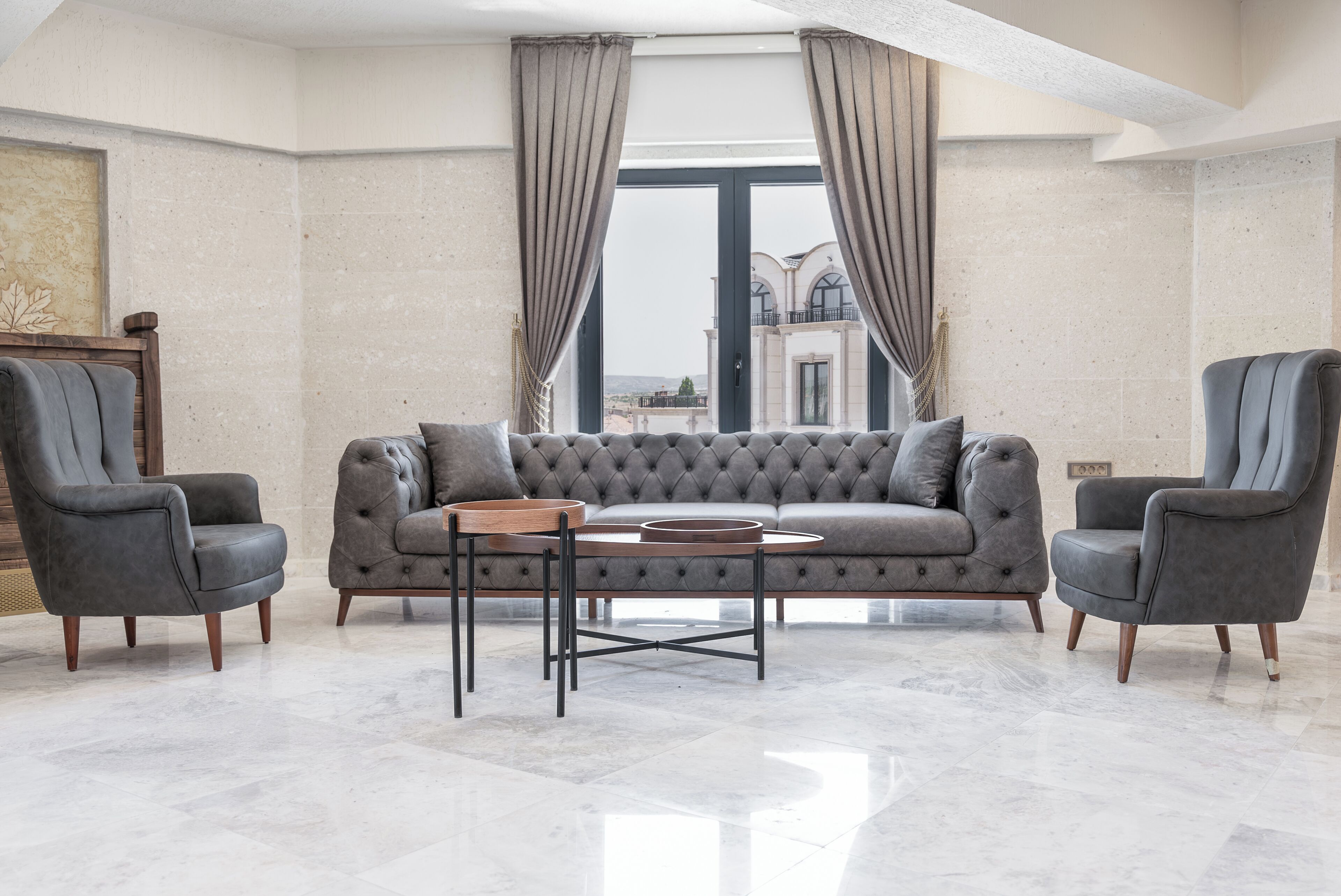 Una sala de estar moderna con un sofá gris, dos sillones y una mesa de centro redonda.