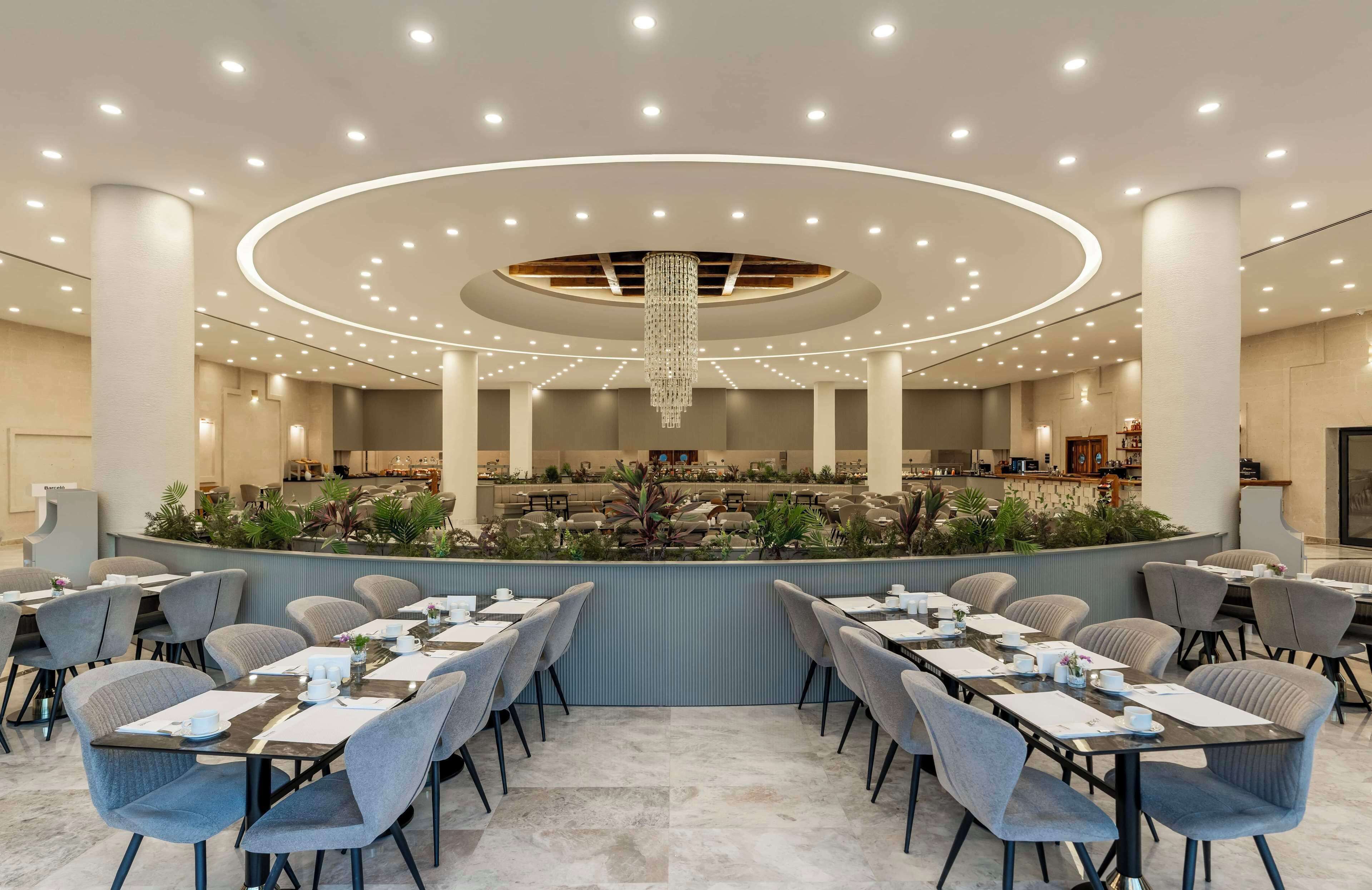 A modern hotel lobby with a central bar area, multiple seating arrangements, and a chandelier.