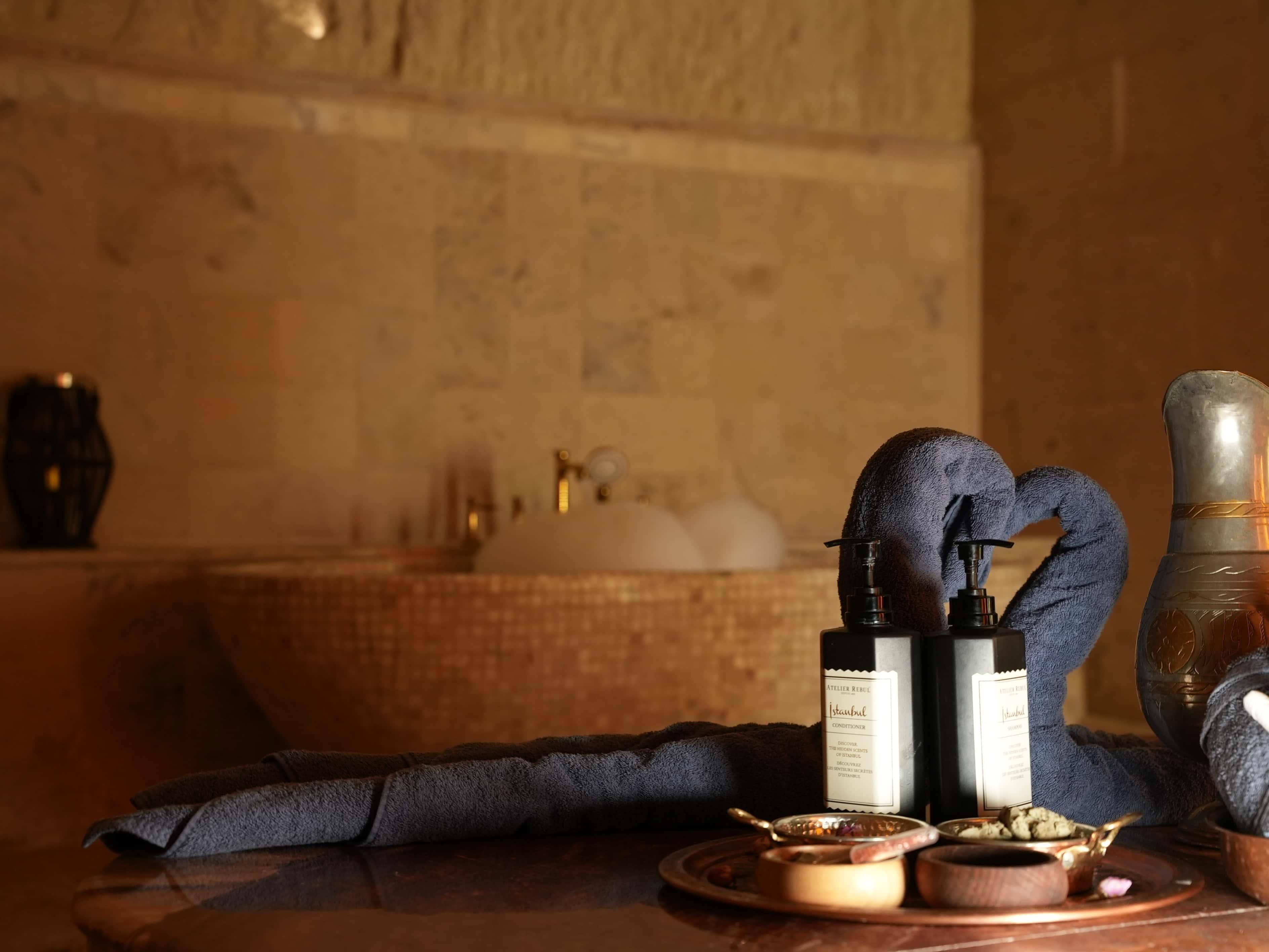 A bathroom with a bathtub, a towel, a bottle of lotion, and a wooden bowl with a spoon.
