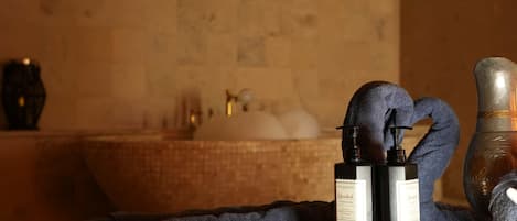 A bathroom with a bathtub, a towel, a bottle of lotion, and a wooden bowl with a spoon.