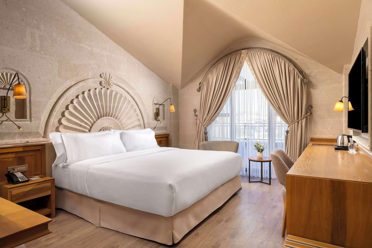 Ein Hotelzimmer mit einem großen Bett, einem Schreibtisch, einem Stuhl und einem kleinen Tisch mit Pflanze.