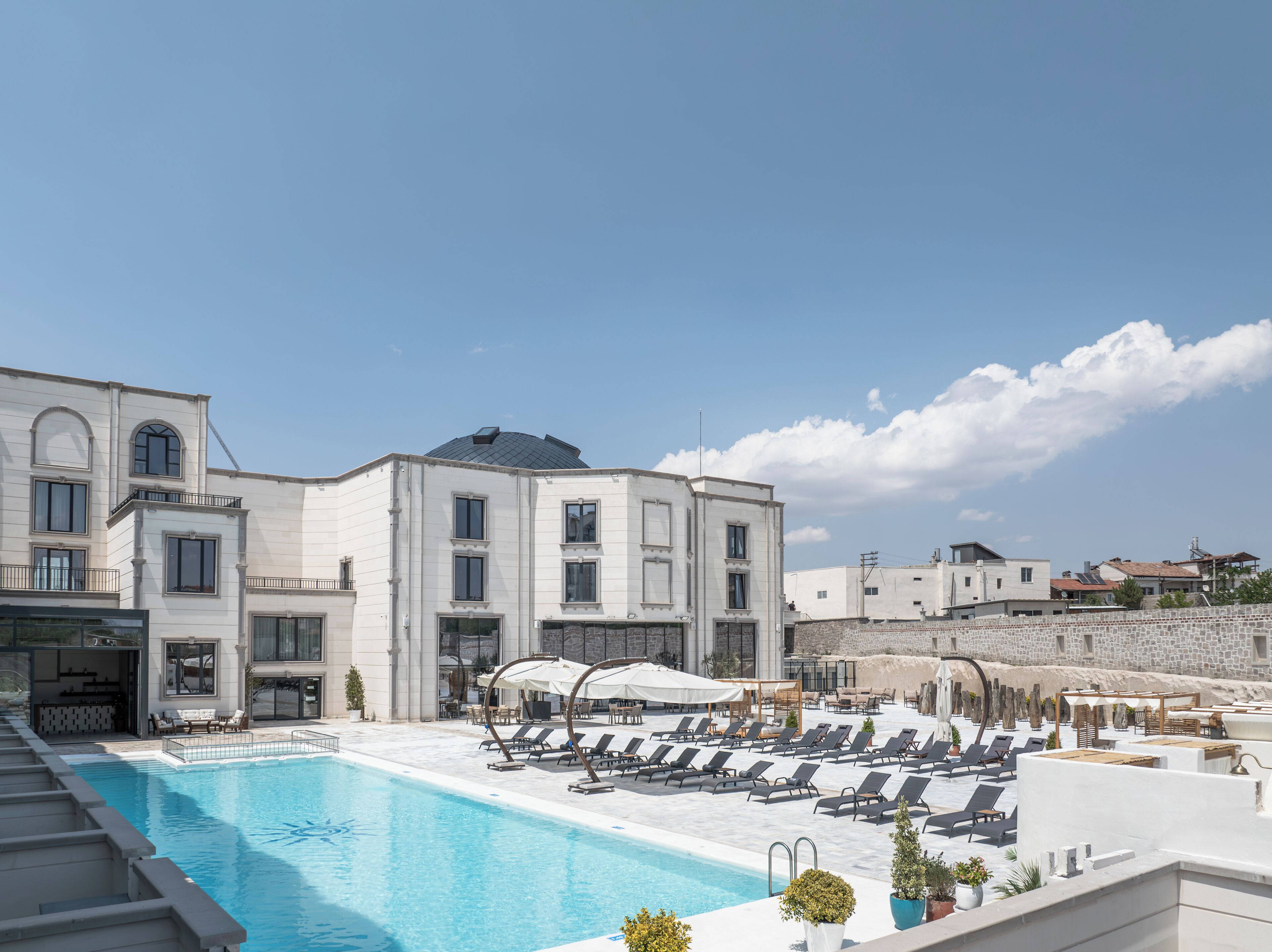 Área de piscina no terraço, com espreguiçadeiras e piscina, cercada por um edifício com cúpula e várias janelas.