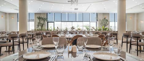 A spacious dining area with multiple tables set for service, large windows, and a chandelier.