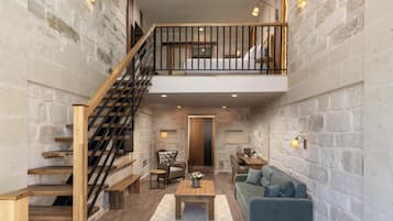A spacious living area with a wooden staircase, a sofa, a coffee table, and a desk with a chair.