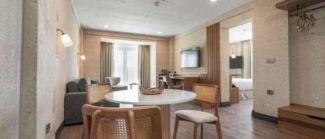 Una habitación de hotel moderna con una mesa de comedor redonda, sillas de madera, un sofá, un televisor y un mueble de madera.