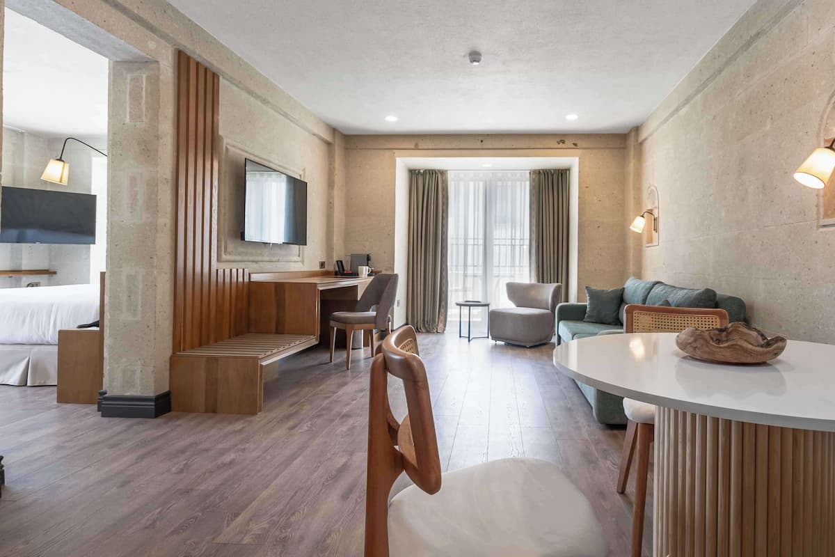 Ein modernes Hotelzimmer mit einer Holzbank, einem runden Esstisch, einer Couch und einem an der Wand montierten Fernseher.
