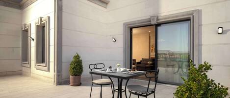 A modern outdoor patio with a table and chairs, a potted plant, and a view of the interior through a glass door.