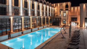 A swimming pool with lounge chairs and a building with arched windows and balconies.