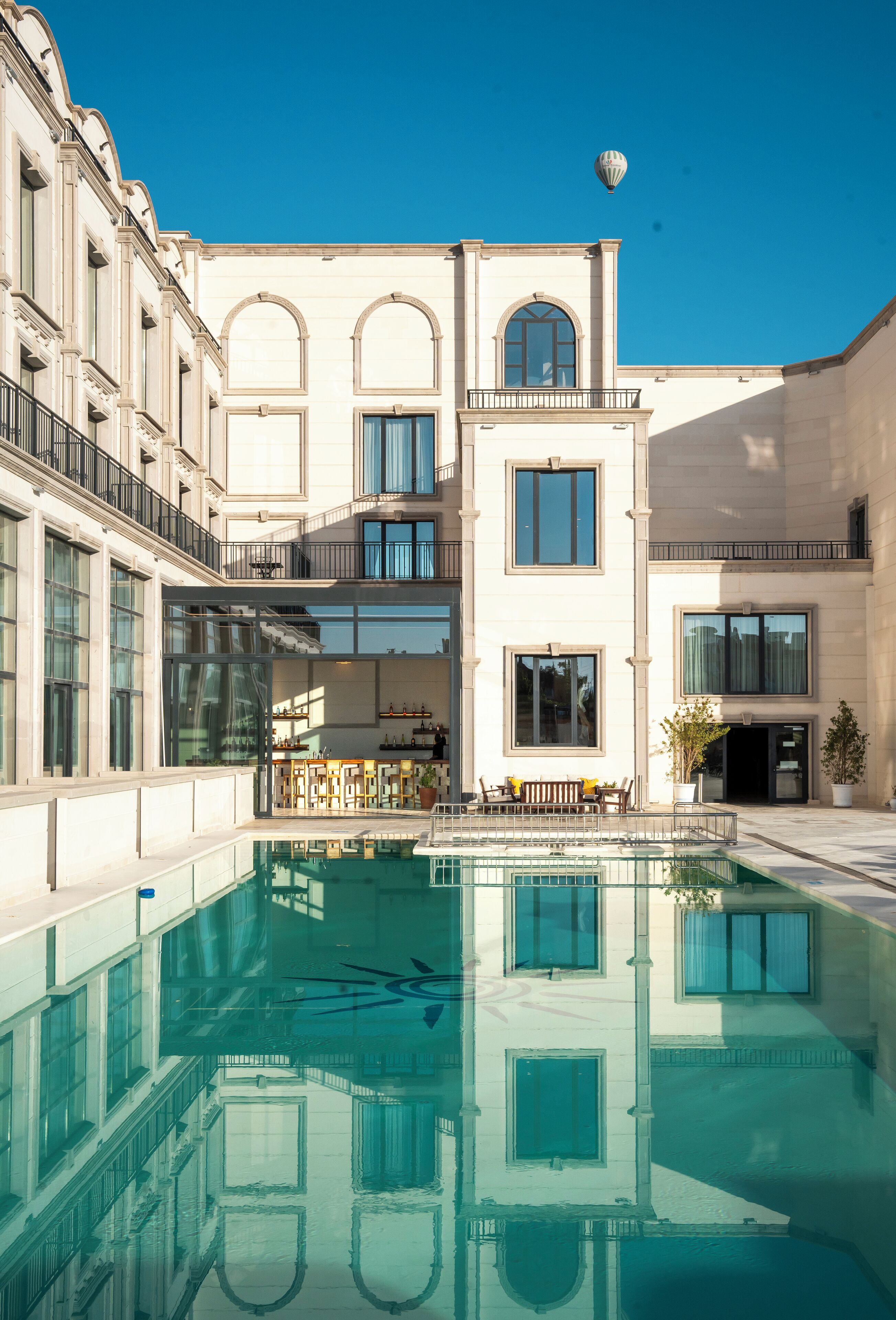 Un patio con piscina, reflejos de edificios y un globo aerostático en el cielo.