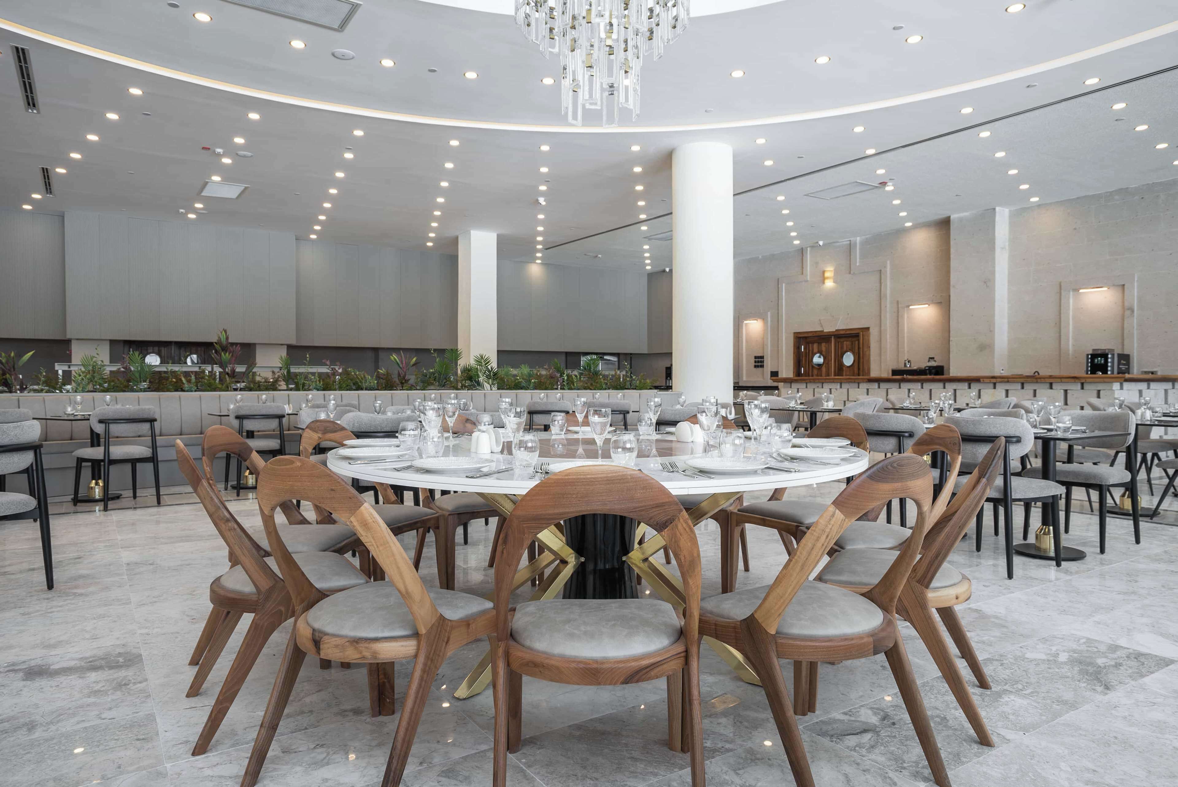 A spacious dining area with round tables set for multiple guests, surrounded by wooden chairs with cushioned seats.