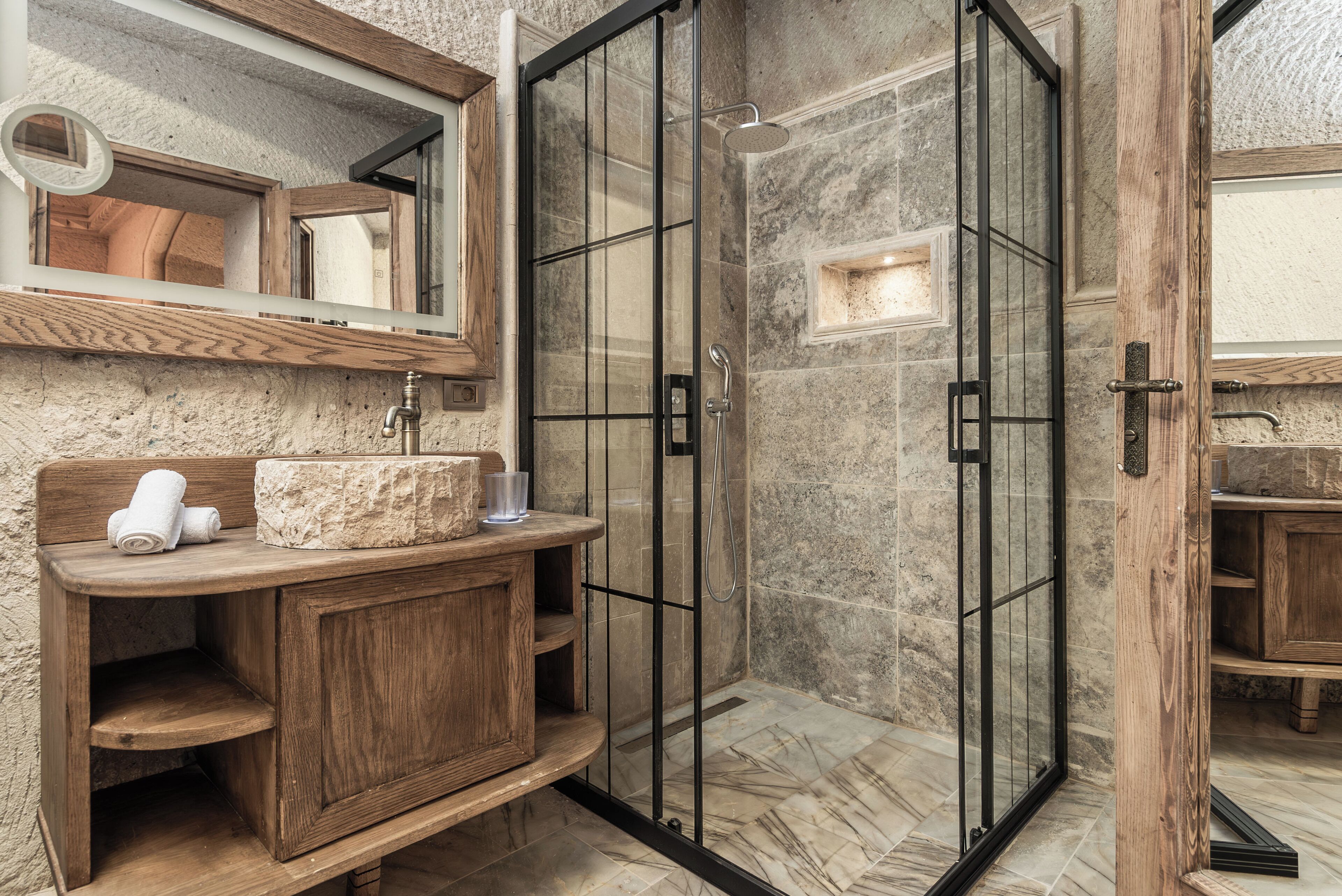 A bathroom with a wooden vanity, a glass shower enclosure, and a marble-tiled floor.