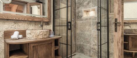 A bathroom with a wooden vanity, a glass shower enclosure, and a marble-tiled floor.