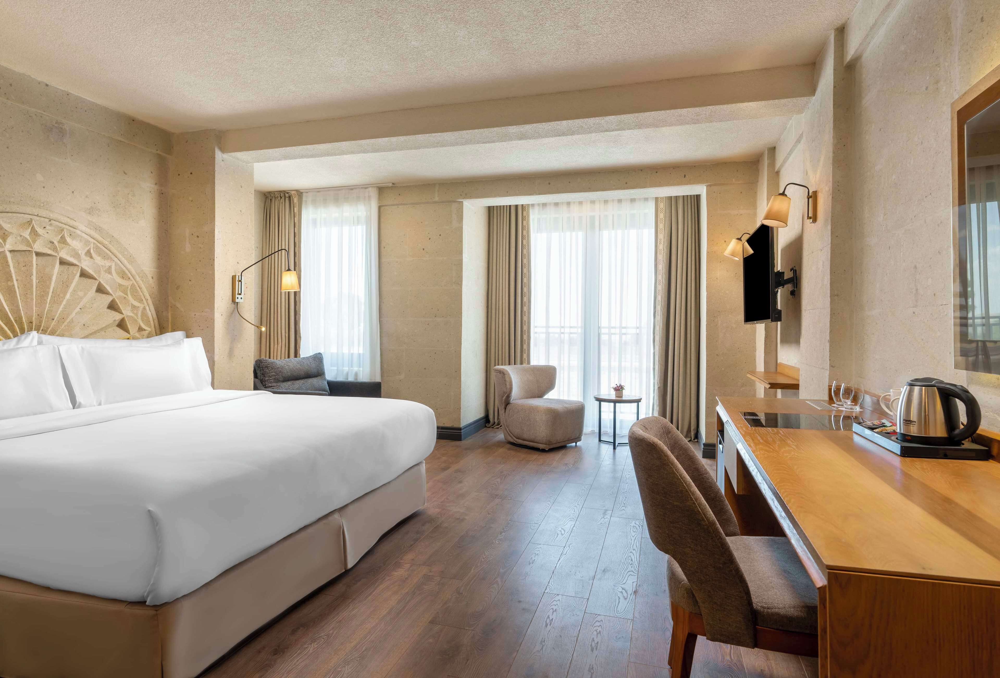 Een hotelkamer met een groot bed, een bureau, een stoel, een klein tafeltje en een lamp.