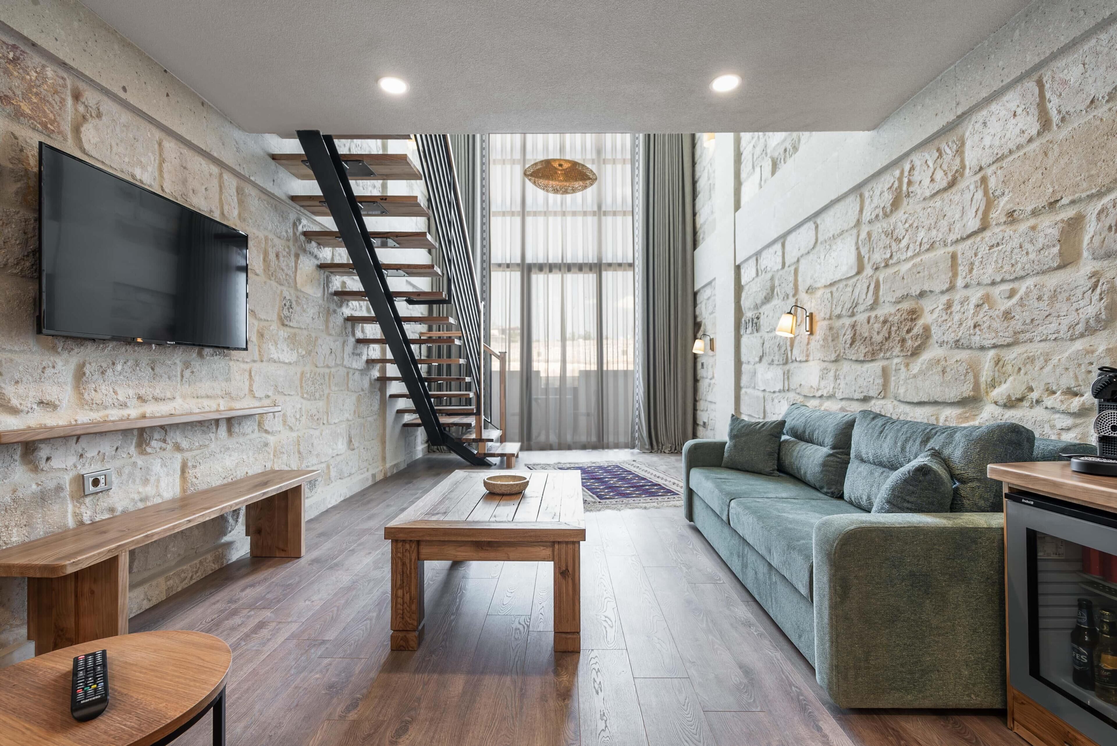 A modern living room with a wooden staircase, a flat-screen TV, a green sofa, and a coffee table.