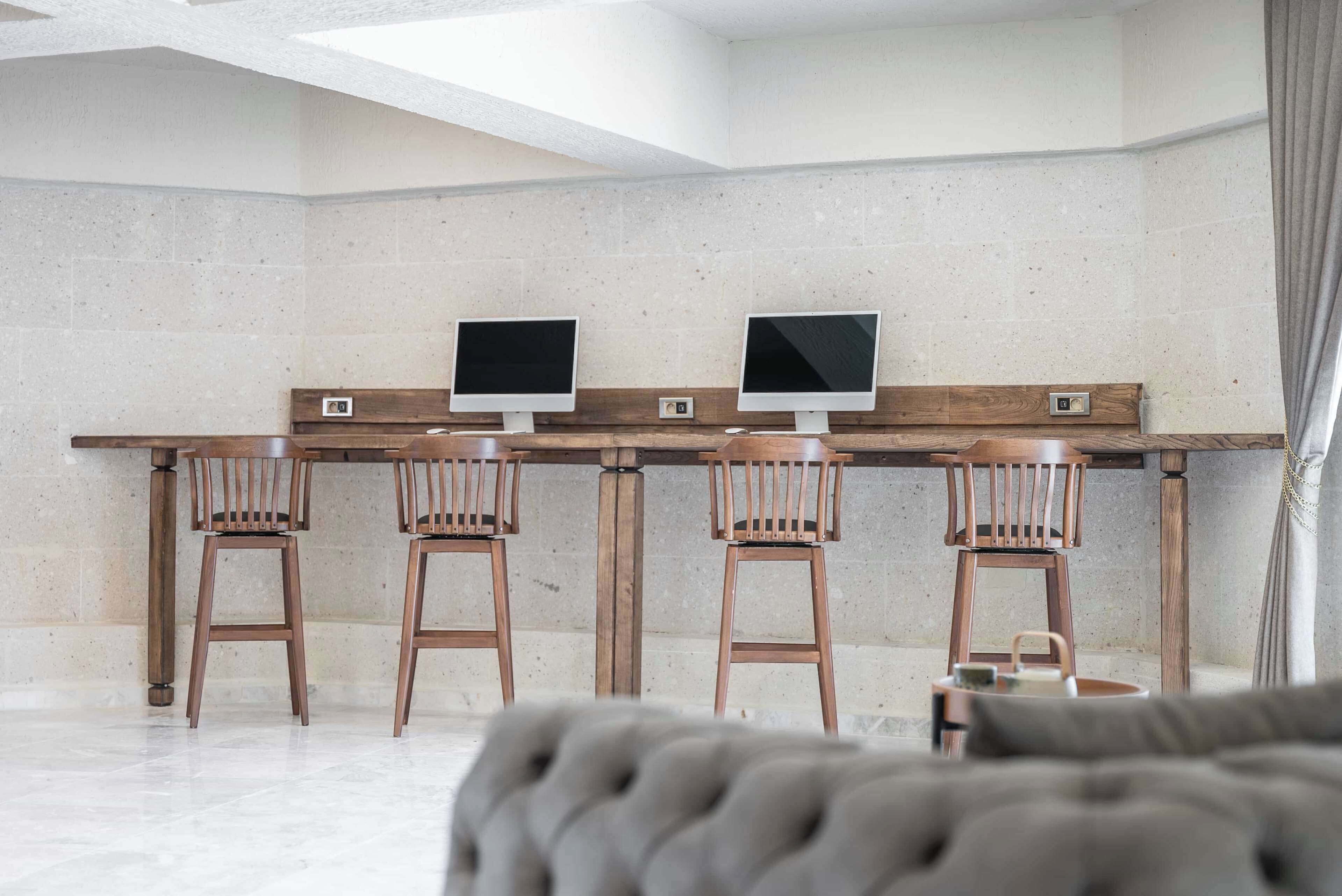 Una habitación moderna con un escritorio de madera largo, dos monitores y cuatro sillas de madera.