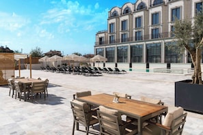 An outdoor patio area with a wooden table and chairs, lounge chairs, and umbrellas.