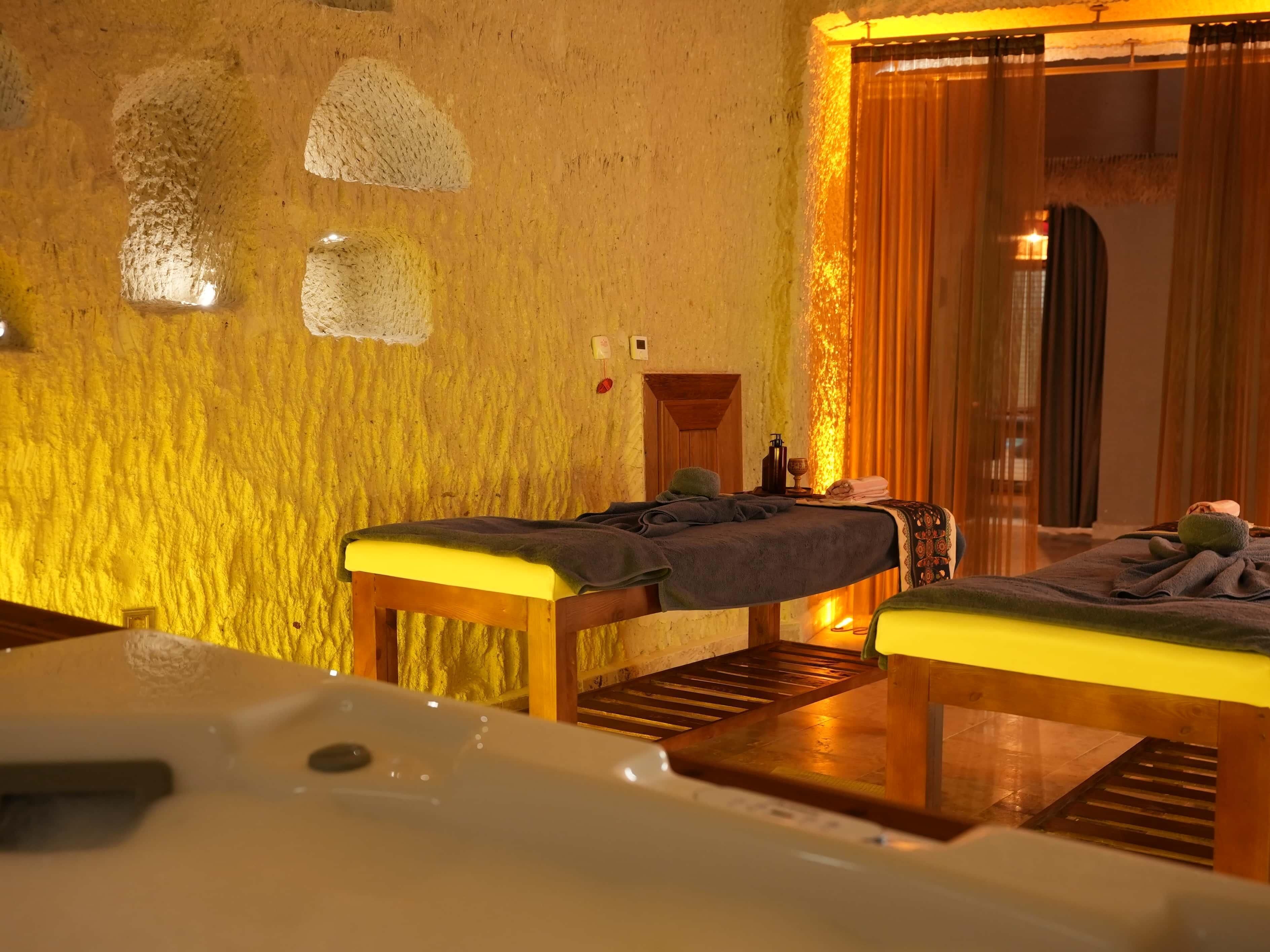 Une salle de spa équipée de deux tables de massage, d’un banc en bois et d’une baignoire.