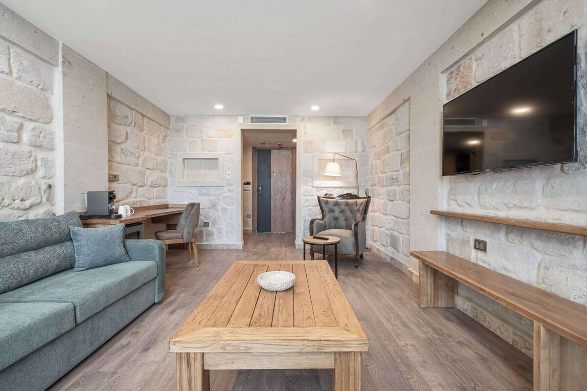 Ein modernes Wohnzimmer mit Steinwand, Flachbildfernseher, Couchtisch aus Holz, einer Couch und einem Schreibtisch mit Stuhl.